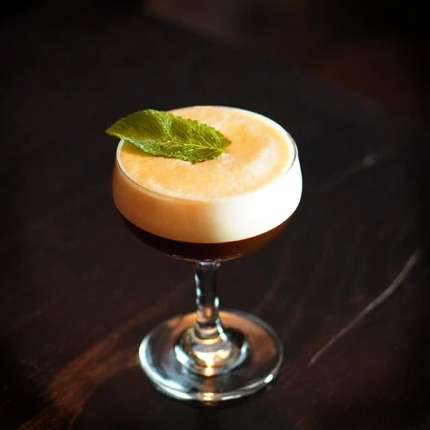 En alkoholfri Espresso Martini med ett tjockt, krämigt skum i ett elegant cocktailglas, garnerad med ett färskt pepparmyntsblad och placerad på en mörk träyta.
