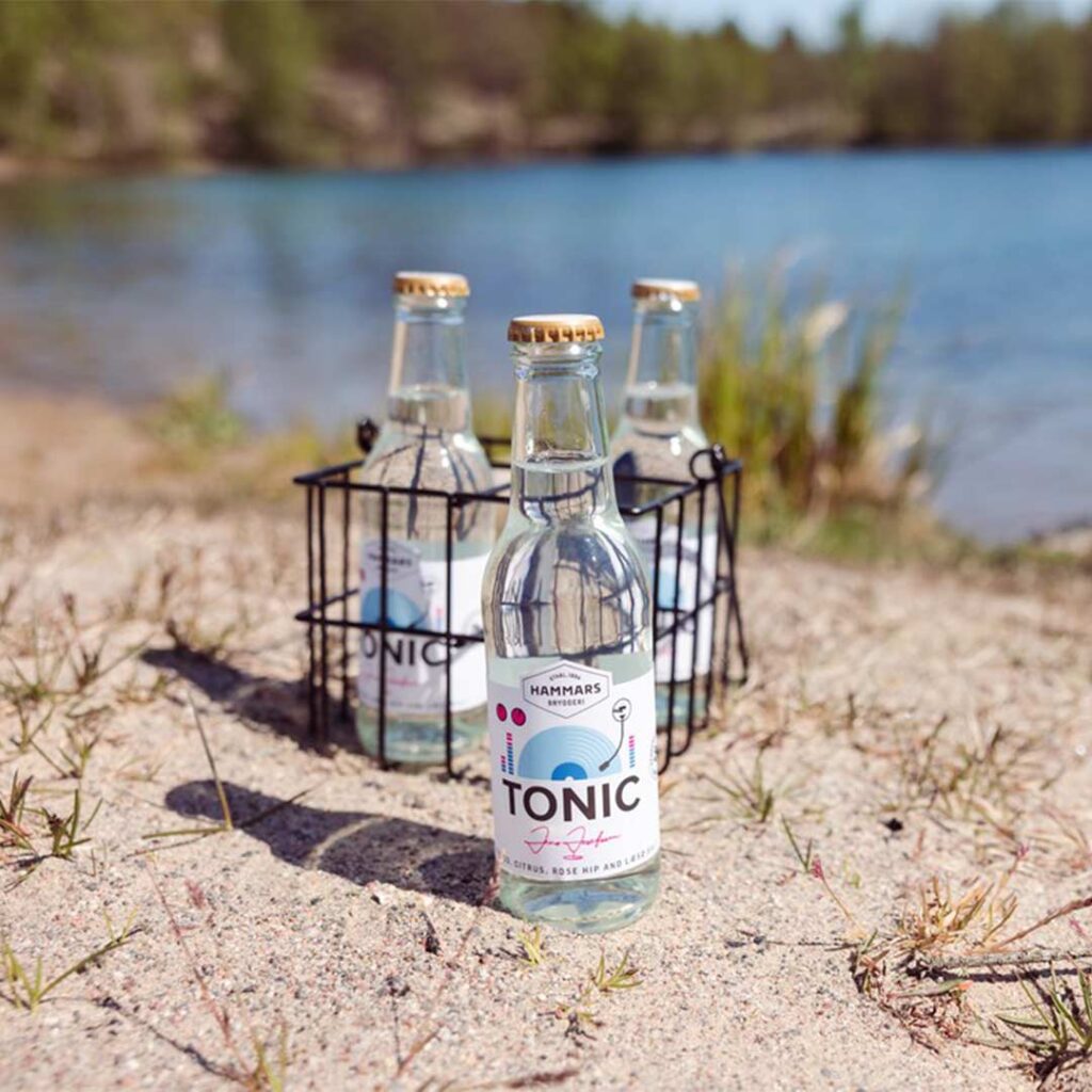 Hammars Bryggeri Tonic Citrus Rose Hip Læsø Salt glasflaskor i sanden på en strand vid vatten